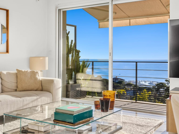 Intérieur d'un appartement moderne avec vue sur la mer, salon lumineux et mobilier contemporain.