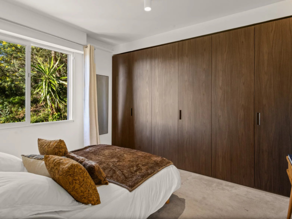 Chambre d'un appartement rénové avec lit et placard en bois, vue sur des plantes à l'extérieur.