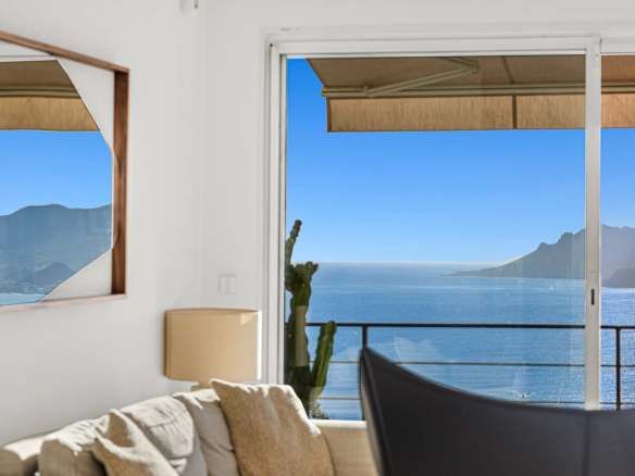 Vue panoramique sur la mer depuis un appartement à Cannes, avec un canapé et des montagnes en arrière-plan.