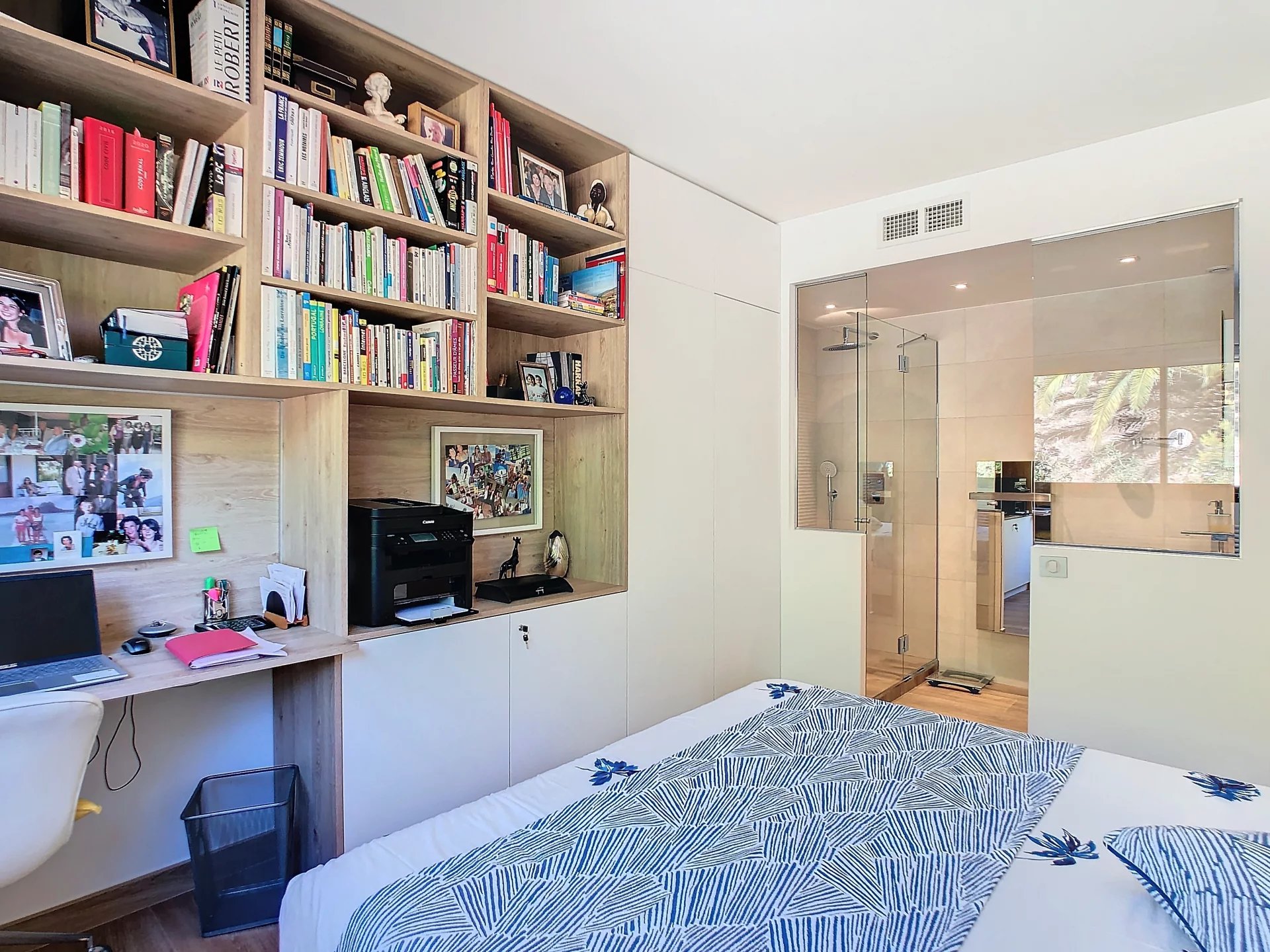 Chambre d'un appartement rénové avec bibliothèque intégrée et salle de bain visible.
