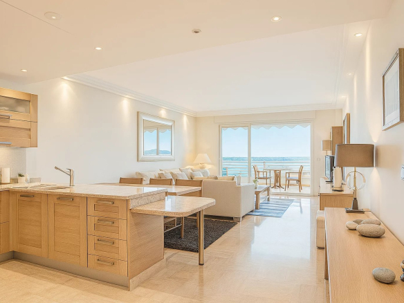 Bright coastal living space with a wood-kitchen island, beige cabinetry, and a seating area facing a balcony with ocean views.