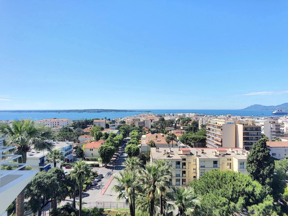 Aerial view of a coastal city with palm trees, orange-tiled roofs, and the blue sea on a sunny day.