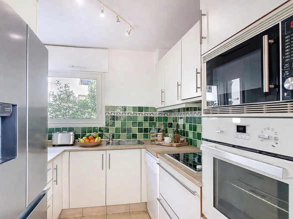 Cuisine moderne équipée avec des appareils électroménagers, carrelage clair et carrelage vert au mur.