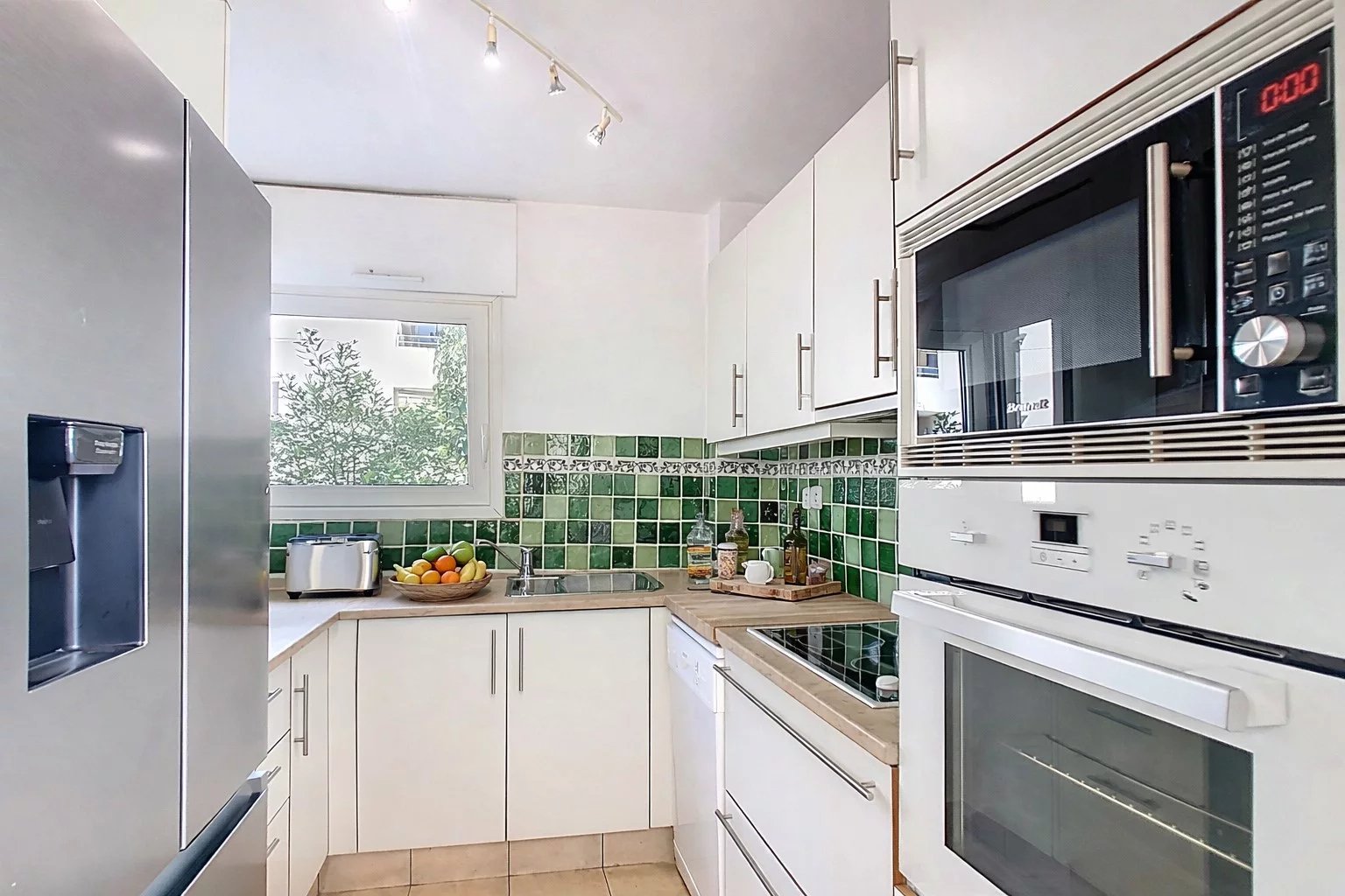 Cuisine moderne équipée avec des appareils électroménagers, carrelage clair et carrelage vert au mur.