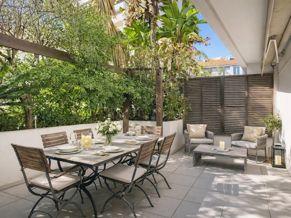 Terrasse d'une maison de ville avec mobilier de jardin, entourée de verdure.