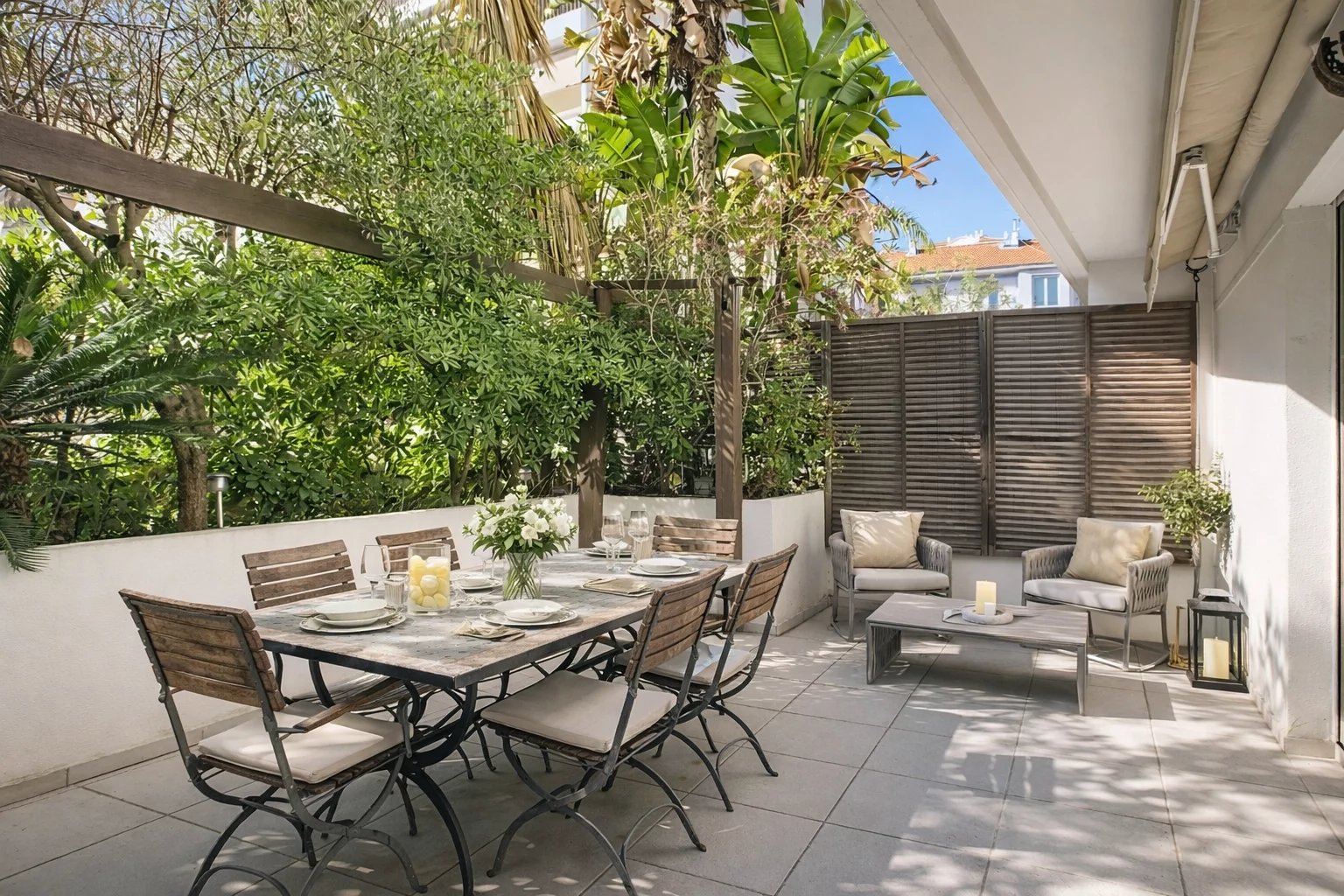 Terrasse d'une maison de ville avec mobilier de jardin, entourée de verdure.