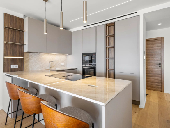 Cuisine moderne et rénovée d'un appartement à Cannes, avec un îlot central et des chaises en bois.