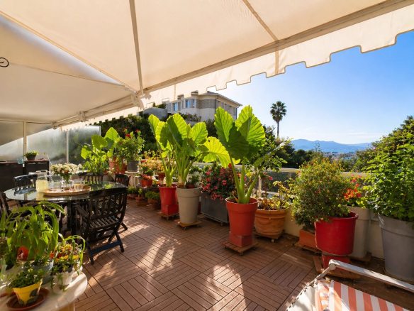 Terrasse d'un appartement à Cannes avec plantes et mobilier de jardin, vue dégagée sur la mer.