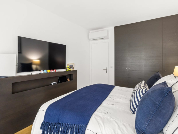 Renovated apartment room with television and bed, decorated with cushions and a blue throw.