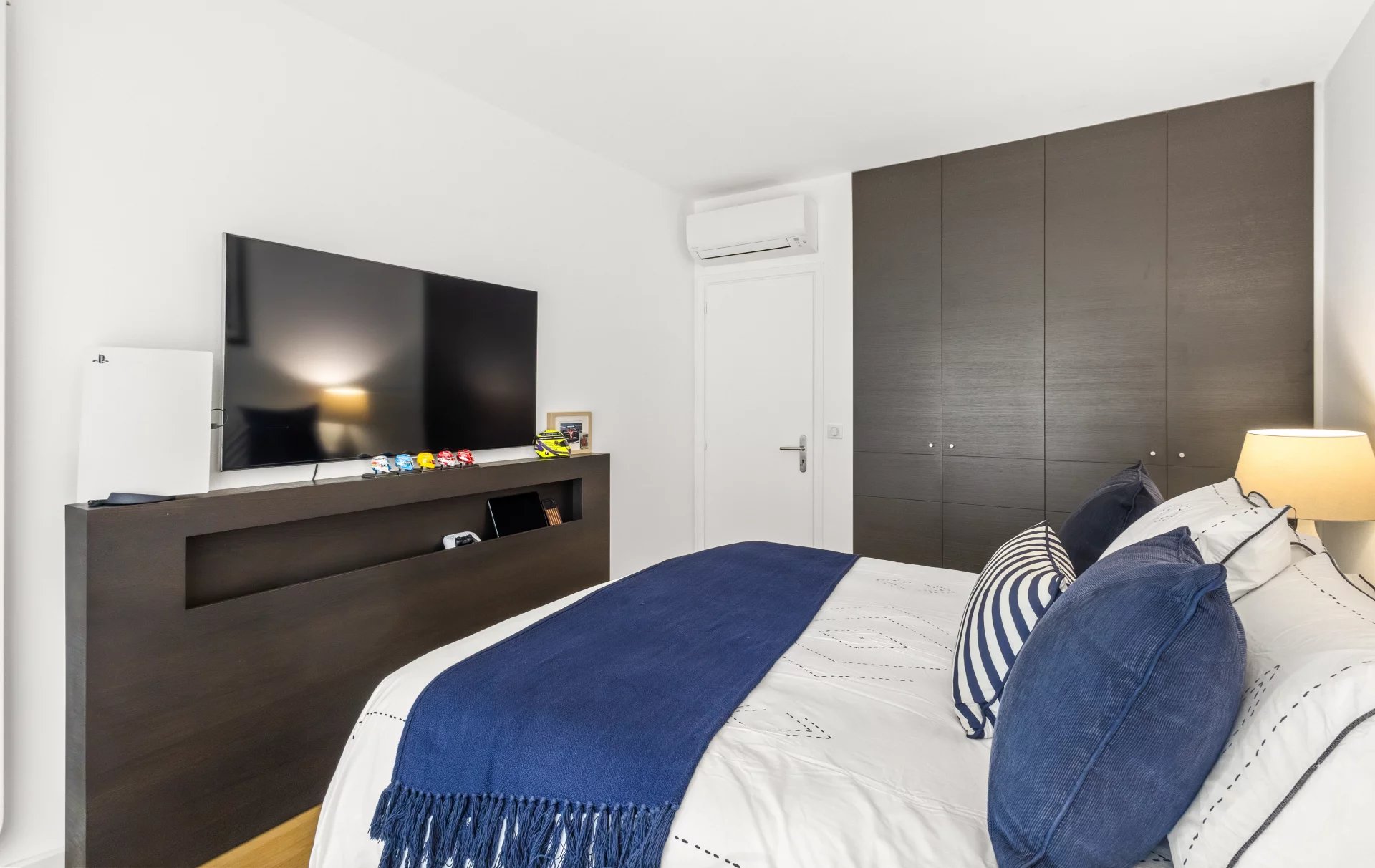 Apartment room in Cannes Renovated apartment room with television and bed, decorated with cushions and a blue throw.
