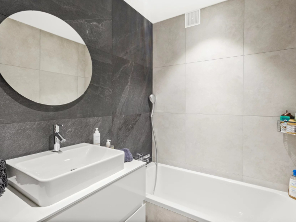 Modern bathroom with bathtub, sink and round mirror.