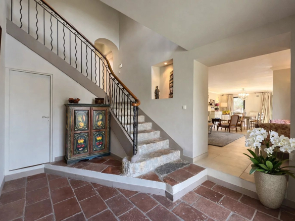 Interior of a villa with a staircase and a living room visible in the background.