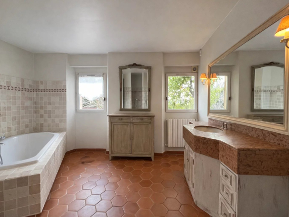 Spacious bathroom with bathtub and sink, terracotta tiles, windows overlooking the outside.