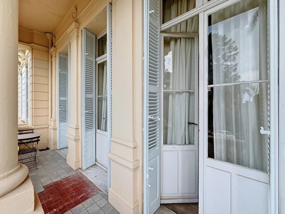 Balcon d'un appartement à Cannes avec portes-fenêtres et vue sur le parc arboré.