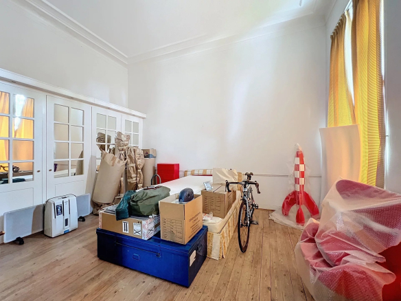 Intérieur d'un appartement à rénover avec des cartons et des objets divers, murs clairs et parquet en bois.