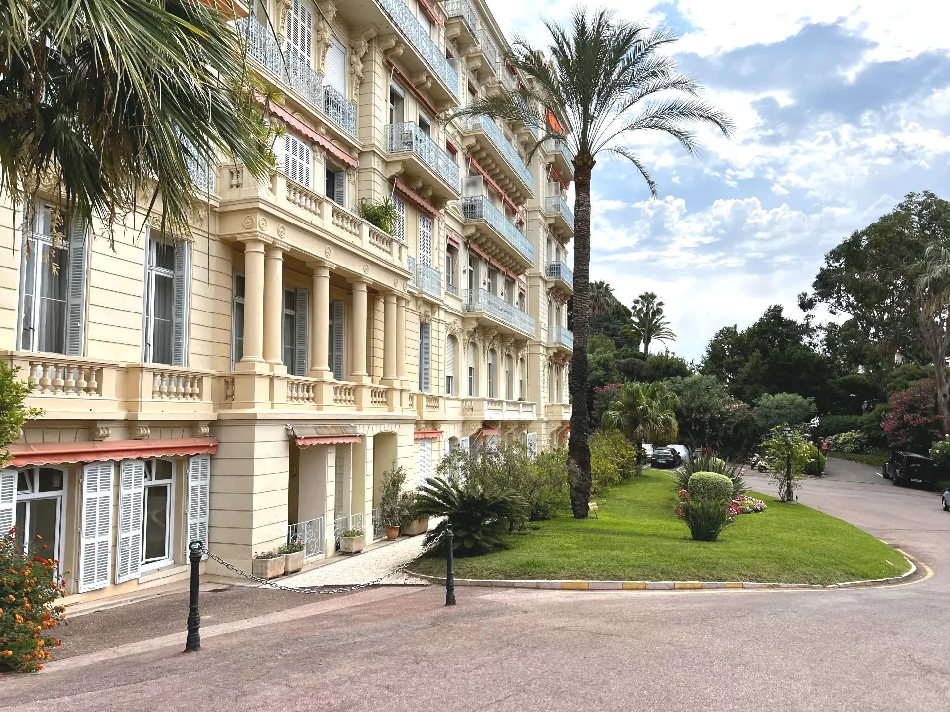 Immeuble de standing à Cannes Façade d'un immeuble de standing à Cannes avec parc arboré et palmiers.