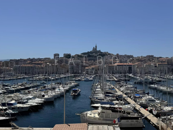 View of the Old Port of Marseille with moored boats and the Notre-Dame de la Garde basilica in the background.