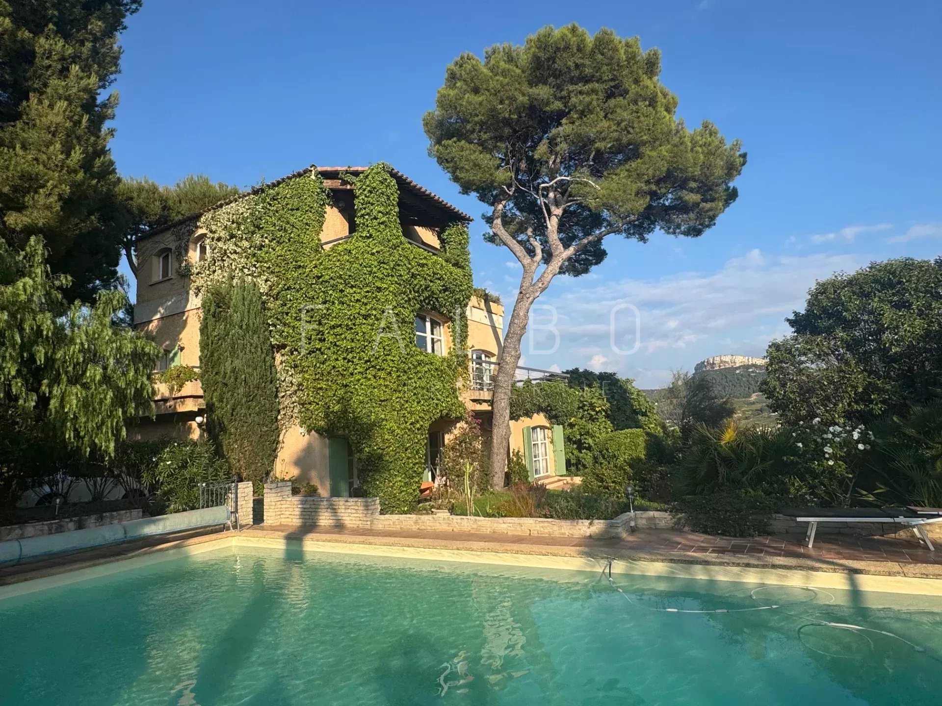 Grande villa avec piscine entourée de verdure à Cassis, vue sur mer et collines.