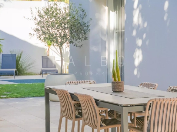 Terrasse d'une villa contemporaine avec table et chaises, jardin et piscine en arrière-plan.