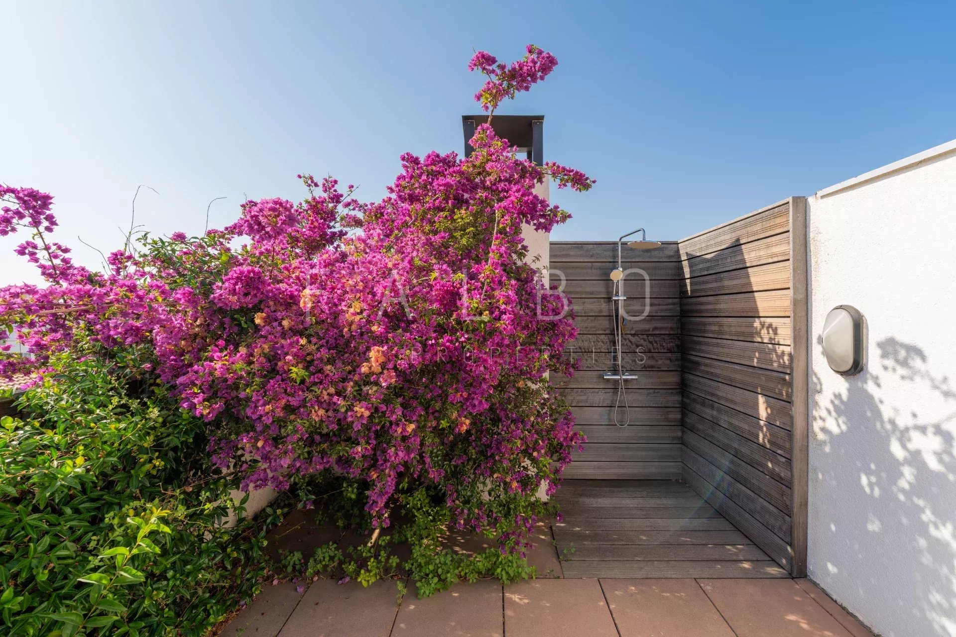 Terrasse d'un appartement avec des fleurs colorées et une douche extérieure.