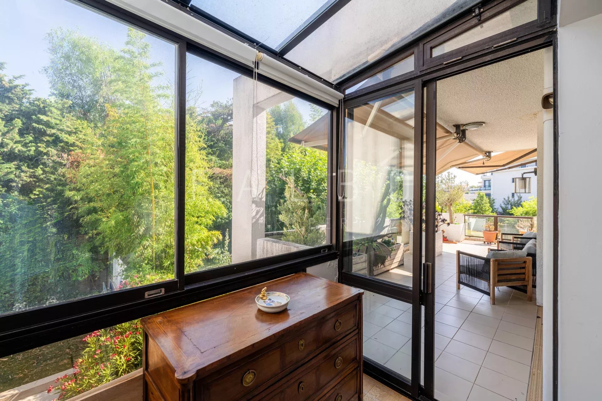 Vue intérieure d'un appartement avec grandes fenêtres donnant sur une terrasse verdoyante à Marseille 8e.