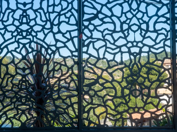 Vue à travers une grille décorative avec un paysage verdoyant en arrière-plan.