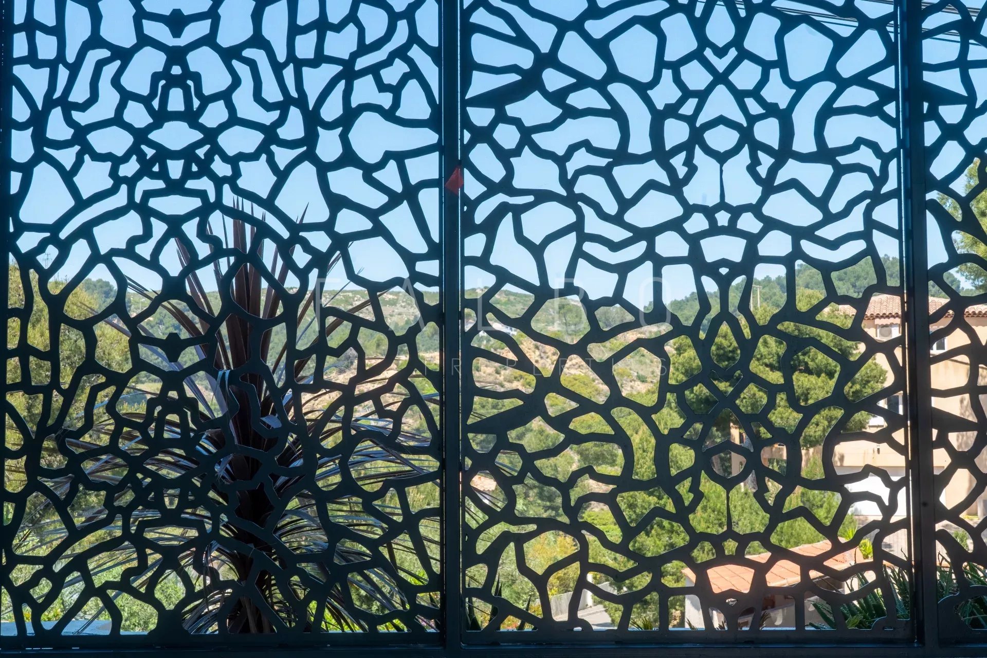 Vue à travers une grille décorative avec un paysage verdoyant en arrière-plan.