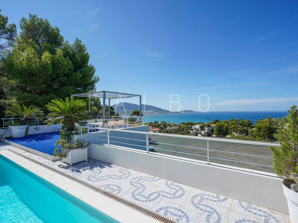 View of a contemporary villa with swimming pool and sea in Marseille, surrounded by greenery.