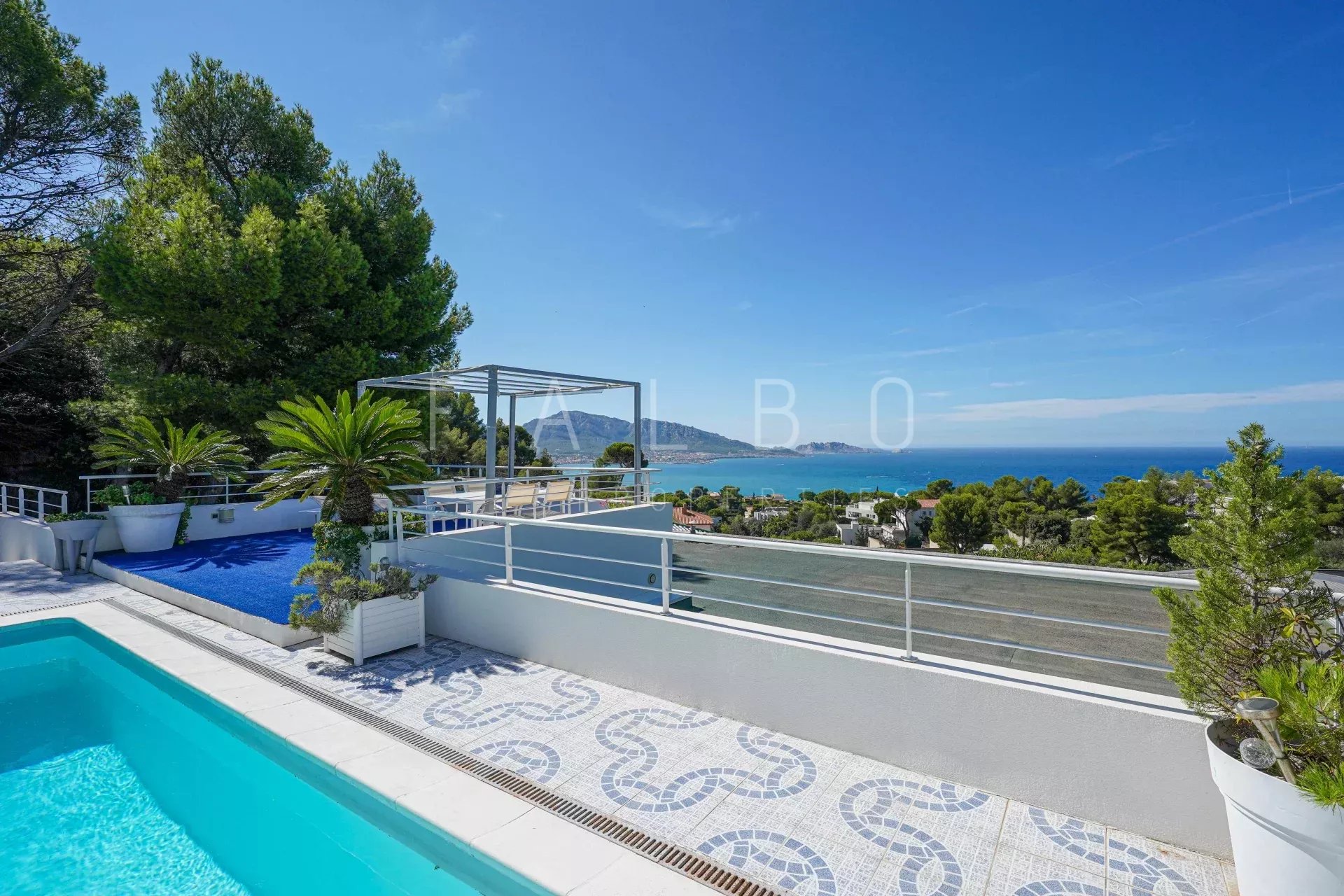 View of a contemporary villa with swimming pool and sea in Marseille, surrounded by greenery.