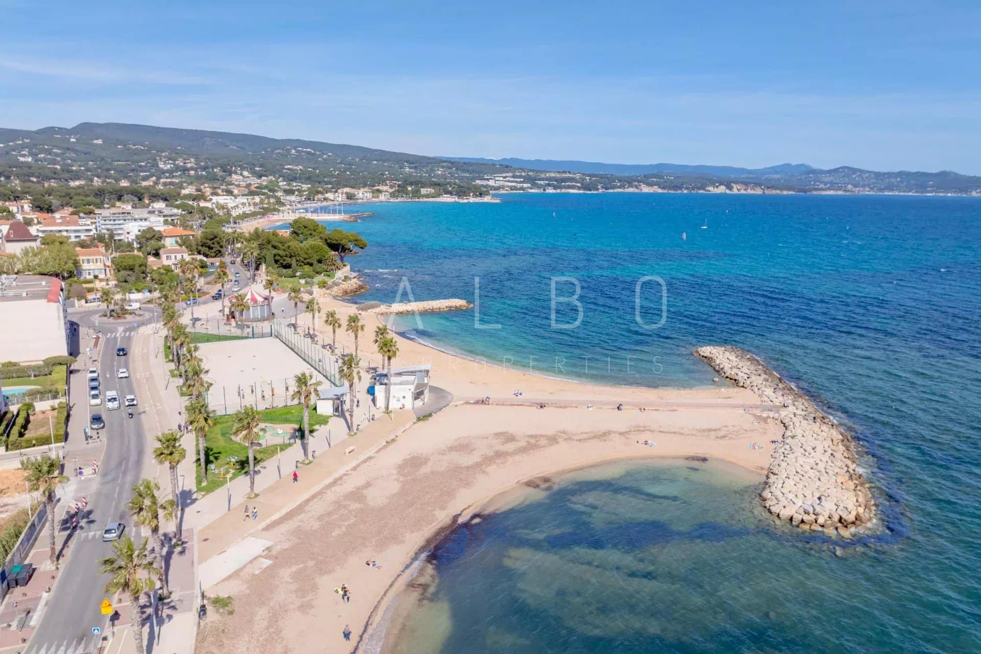 Plage de La Ciotat Vue aérienne de la plage et de la promenade à La Ciotat, avec des palmiers et des bâtiments en arrière-plan.