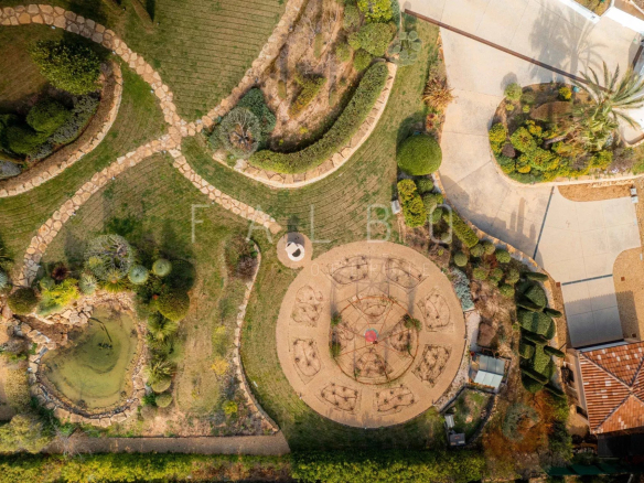 Vue aérienne d'un parc paysager avec cheminements et aménagements, villa en arrière-plan.