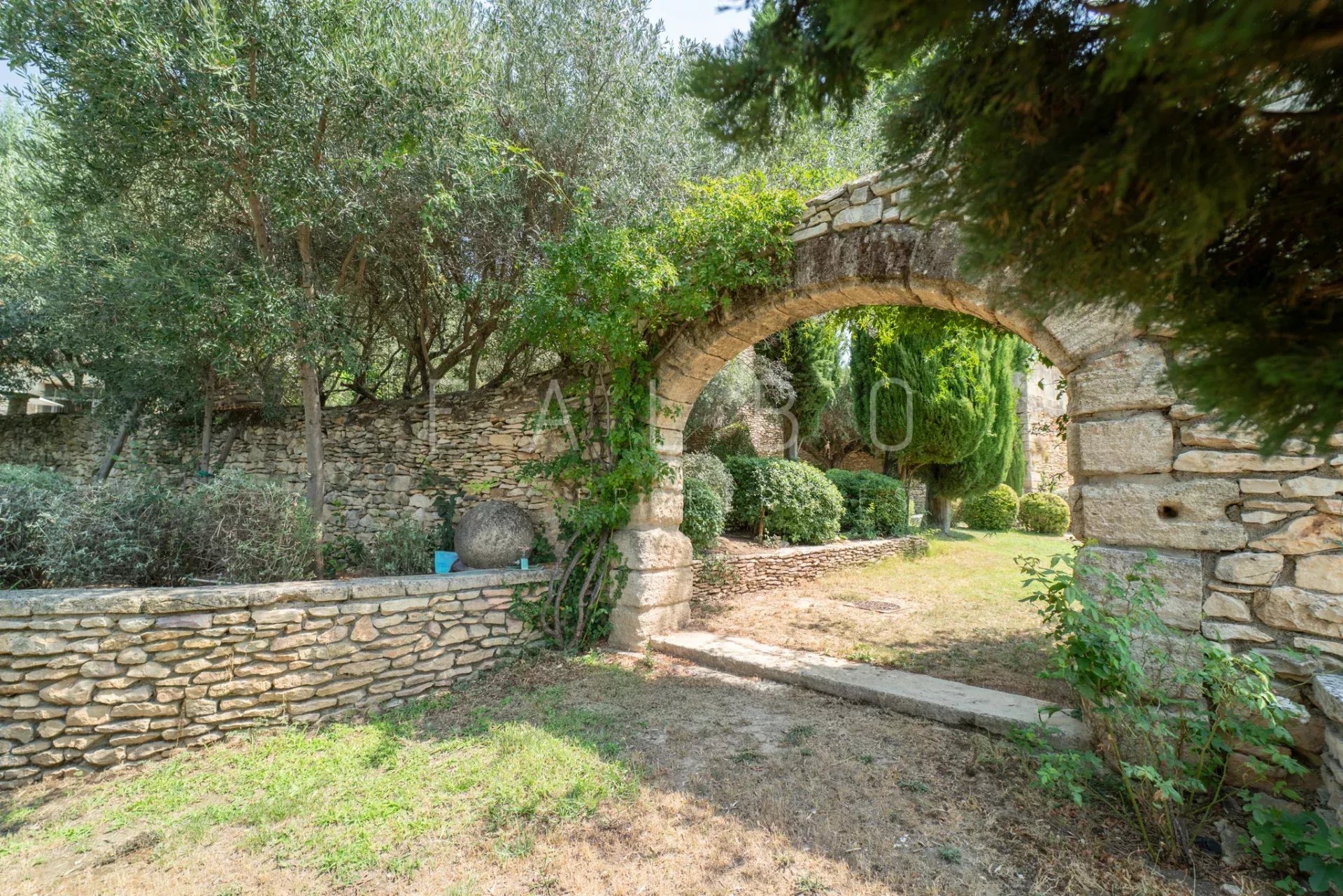 Garden of a stone farmhouse Entrance to a landscaped garden with a stone arch, 400m² farmhouse in Saint-Maximin near Uzès.