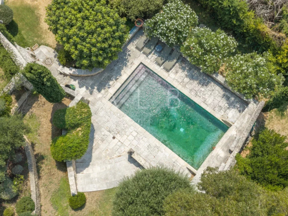 Aerial view of a swimming pool surrounded by landscaped gardens in a stone farmhouse.
