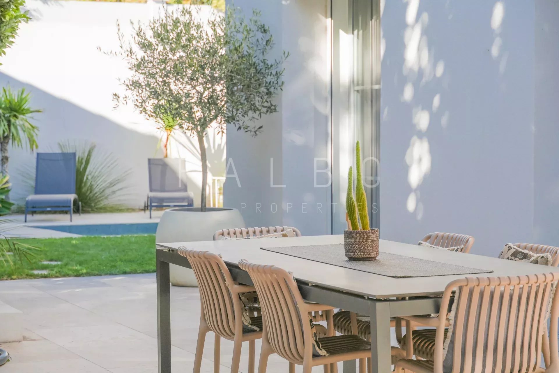 Terrasse d'une villa contemporaine avec table et chaises, jardin et piscine en arrière-plan.