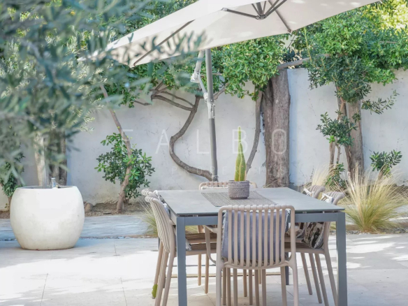 Terrasse d'une villa contemporaine avec table et chaises, ombragée par un parasol et entourée de verdure.