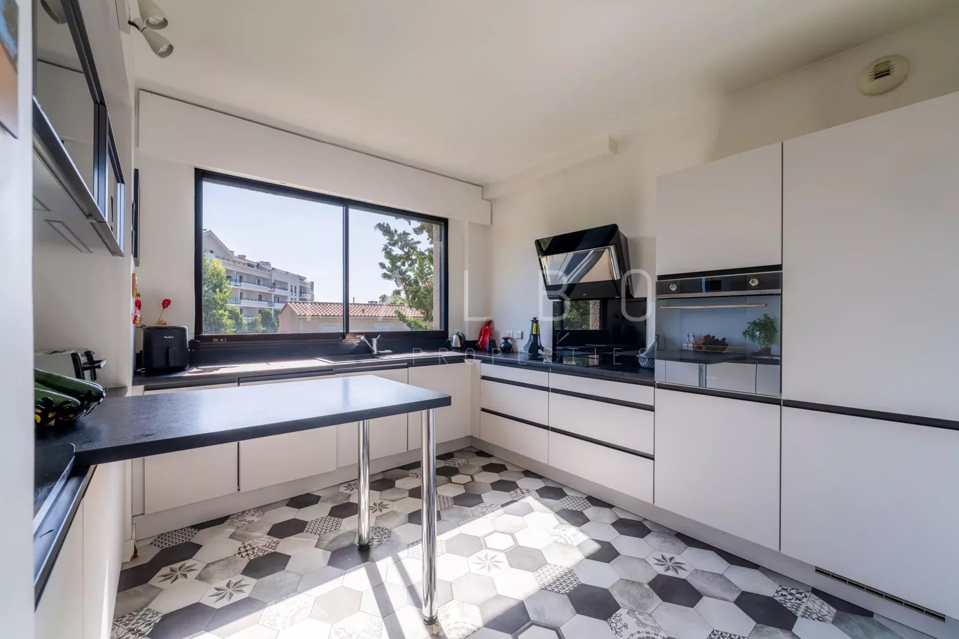 Cuisine moderne dans un appartement à Marseille 8e Cuisine moderne avec fenêtres et vue sur l'extérieur, carrelage noir et blanc.