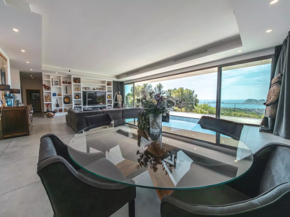 Intérieur d'une villa contemporaine avec vue sur la mer, table ronde en verre et grandes baies vitrées.