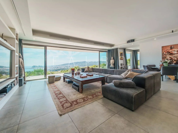Intérieur moderne d'une villa avec vue sur la mer, grandes fenêtres et mobilier contemporain.