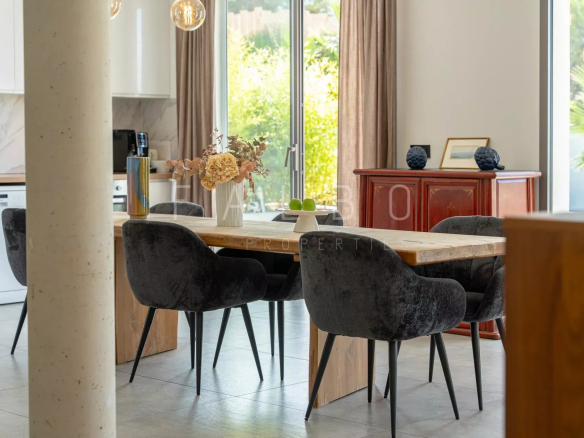 Salle à manger moderne avec table en bois et chaises noires, éclairage suspendu, vue sur le jardin.