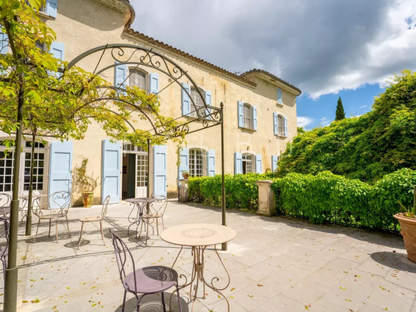 Terrasse d'un château restauré avec tables et chaises, entourée de verdure.