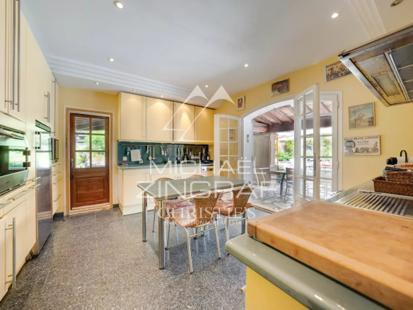 Bright kitchen with yellow walls, white cabinets, stainless appliances, a small table and wicker chairs, and French doors to an outdoor patio.