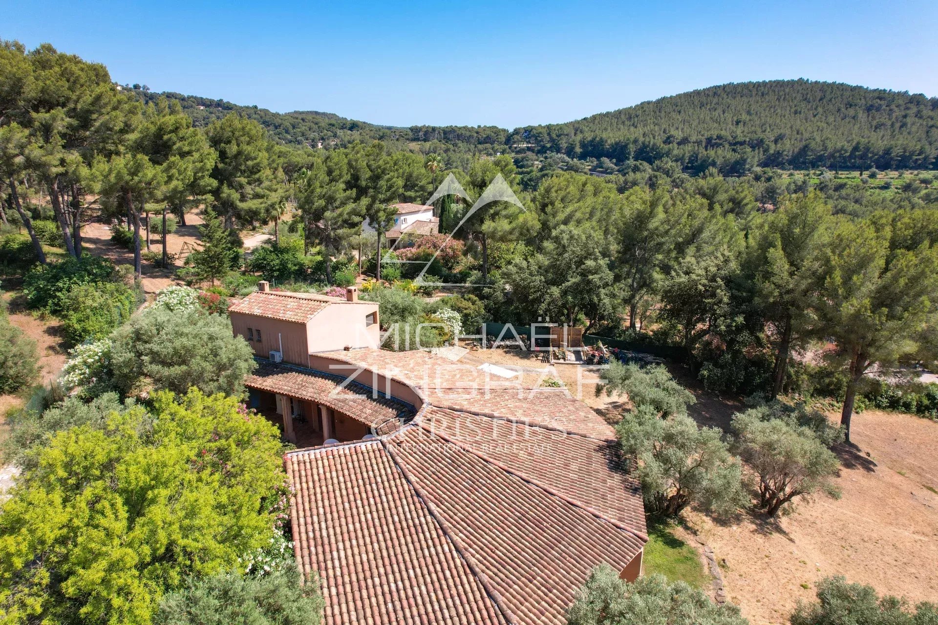 Aerial view of a terracotta-roof villa surrounded by pine trees in a sunny countryside setting