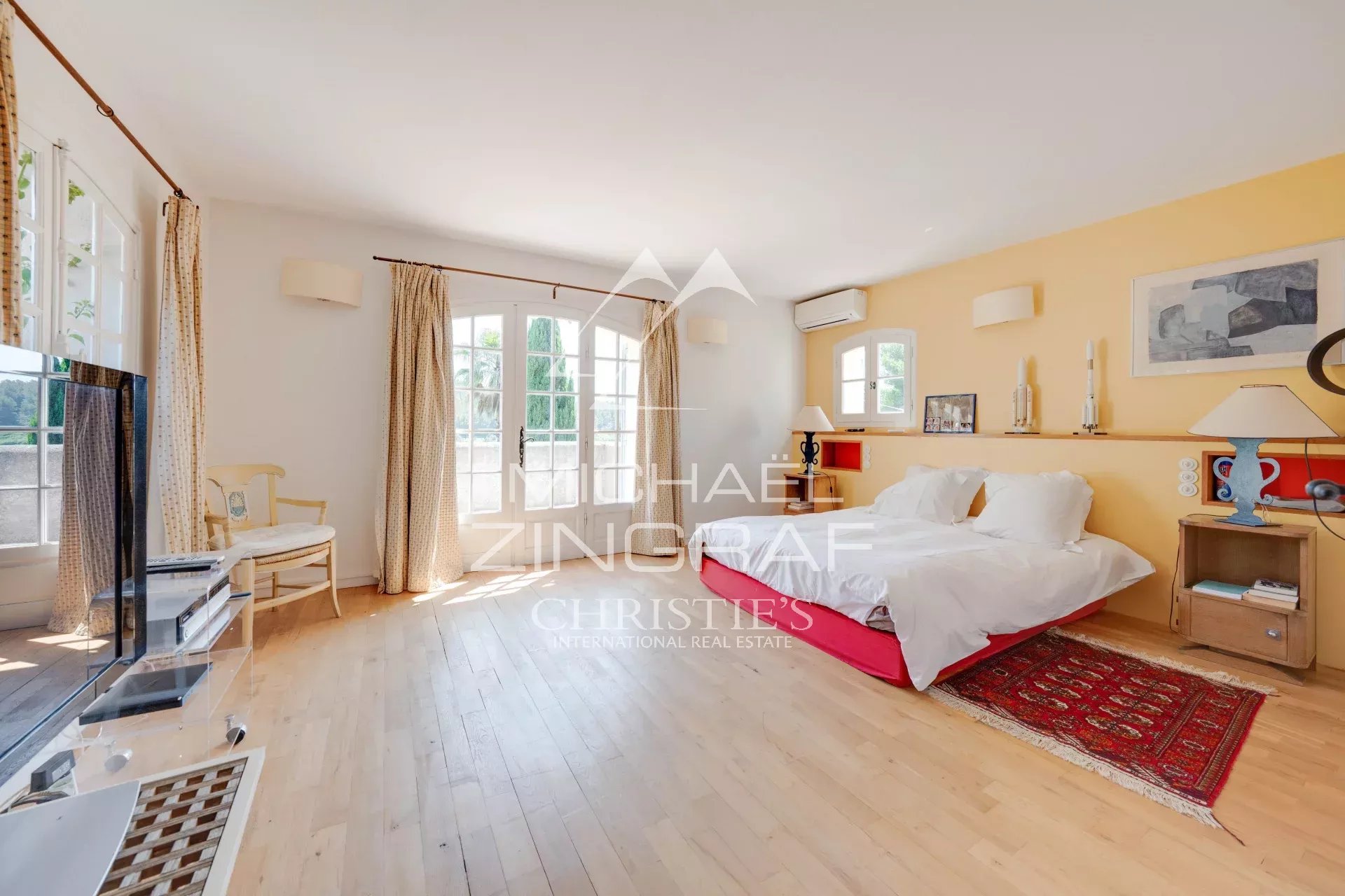 Bright, spacious bedroom with a white-bedding bed on a red bed base, yellow accent wall, wooden floor, and matching nightstands.