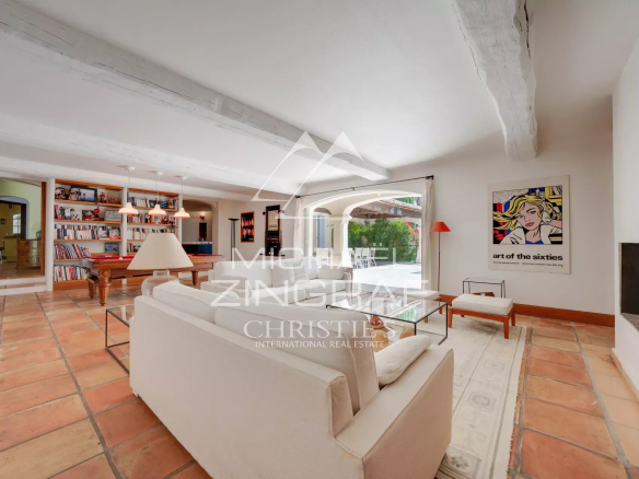 Bright living room with white sofas, glass coffee table, terracotta tile floor, and a bookshelf wall in the background.