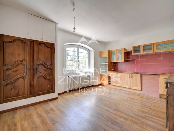 Rustic kitchen with wooden cabinets and a red tile backsplash, arched window, and large carved doors on the left.