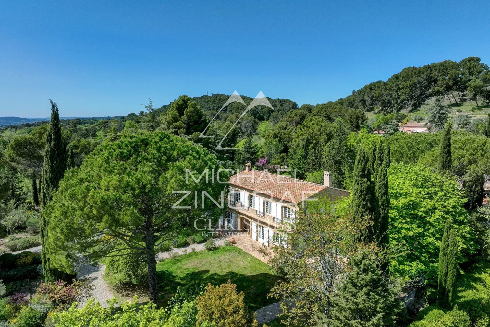 Charming hillside villa surrounded by tall trees and lush greenery under a clear blue sky