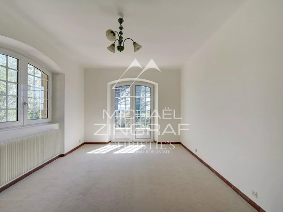 Bright, empty living room with white walls, a curved arched window/door at the far end, and a radiator along the left wall, lit by natural daylight.