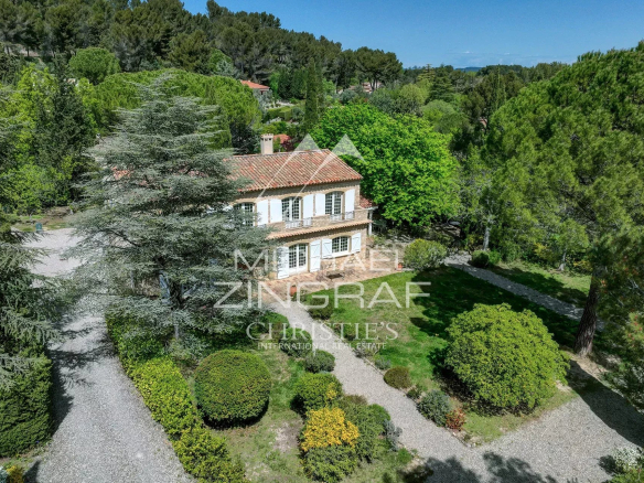 Two-story stone villa with a terracotta roof, white shutters, and a manicured gravel driveway tucked among tall trees and lush greenery outside. (Property listing)
