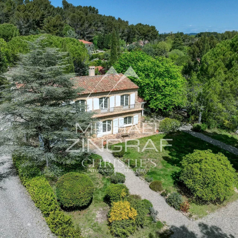Two-story stone villa with a terracotta roof, white shutters, and a manicured gravel driveway tucked among tall trees and lush greenery outside. (Property listing)