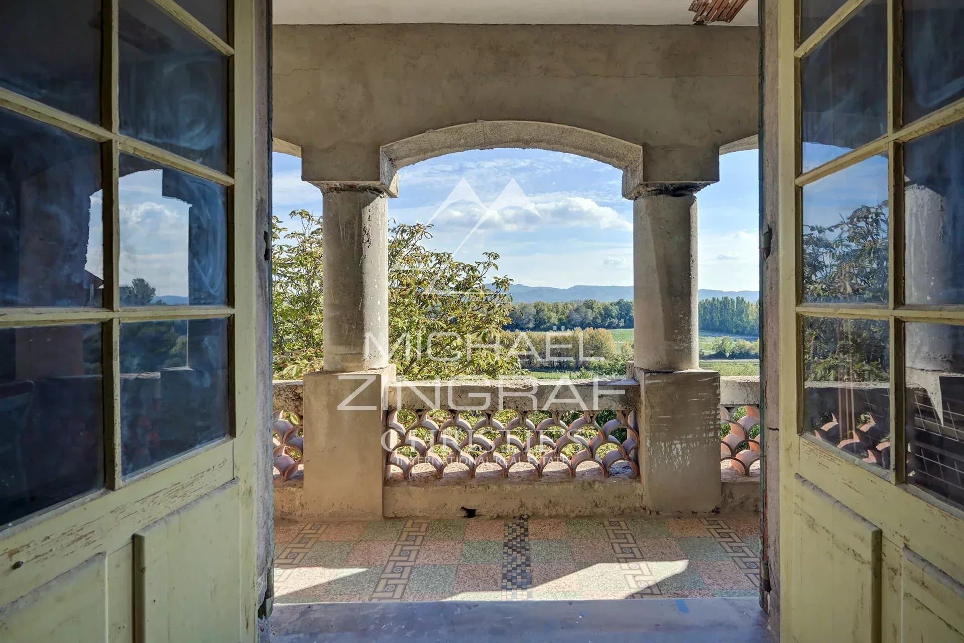 Vue depuis un balcon avec colonnes, offrant un panorama sur la nature environnante.
